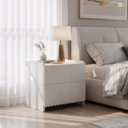 Nasrin 2 Drawer Bedside Table in White, featuring modern design with subtle ribbed drawer fronts, topped with a vase, books, and lamp, elegantly set in a softly lit bedroom corner.