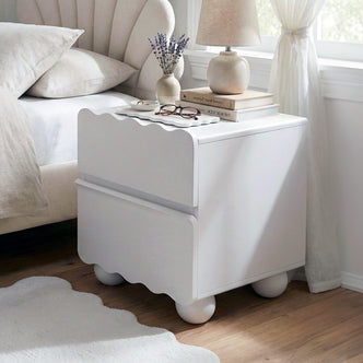 White nightstand beside a bed with lamp and decor in a bright bedroom