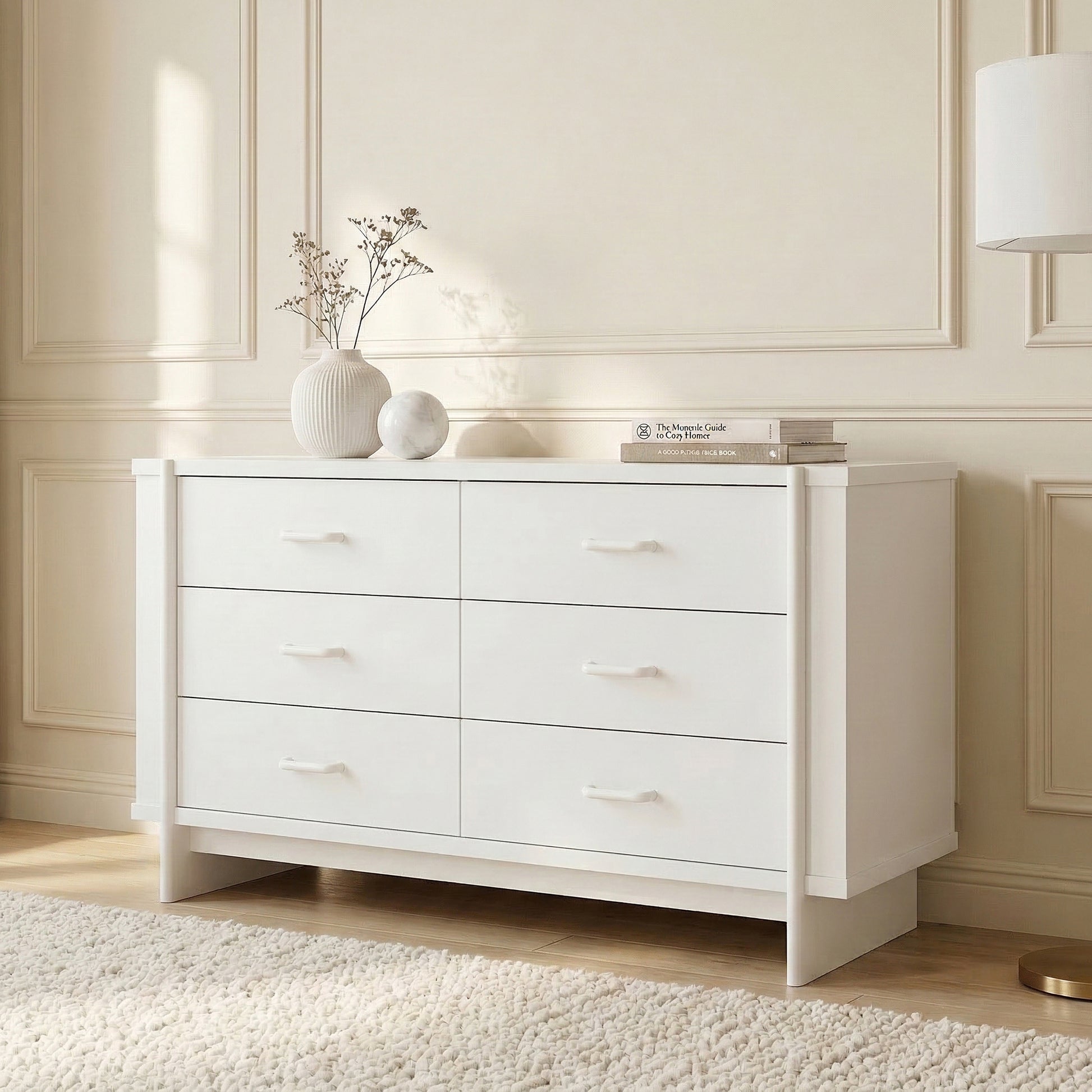 White six-drawer dresser in a styled room with decorative vase, books, rug, and wall paneling