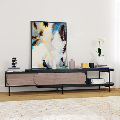 Novia 220-270cm Extendable Entertainment TV Unit in Black, featuring a black metal frame, wooden sliding doors, and a modern display with books, vases, a camera, and an orchid on top.