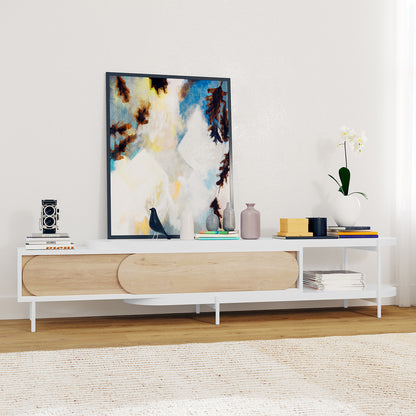 Novia 220-270cm Extendable Entertainment TV Unit in White, featuring sliding oval-fronted wooden doors, open cubby with magazines, slender white legs, and a chic top adorned with books, art, and decor.