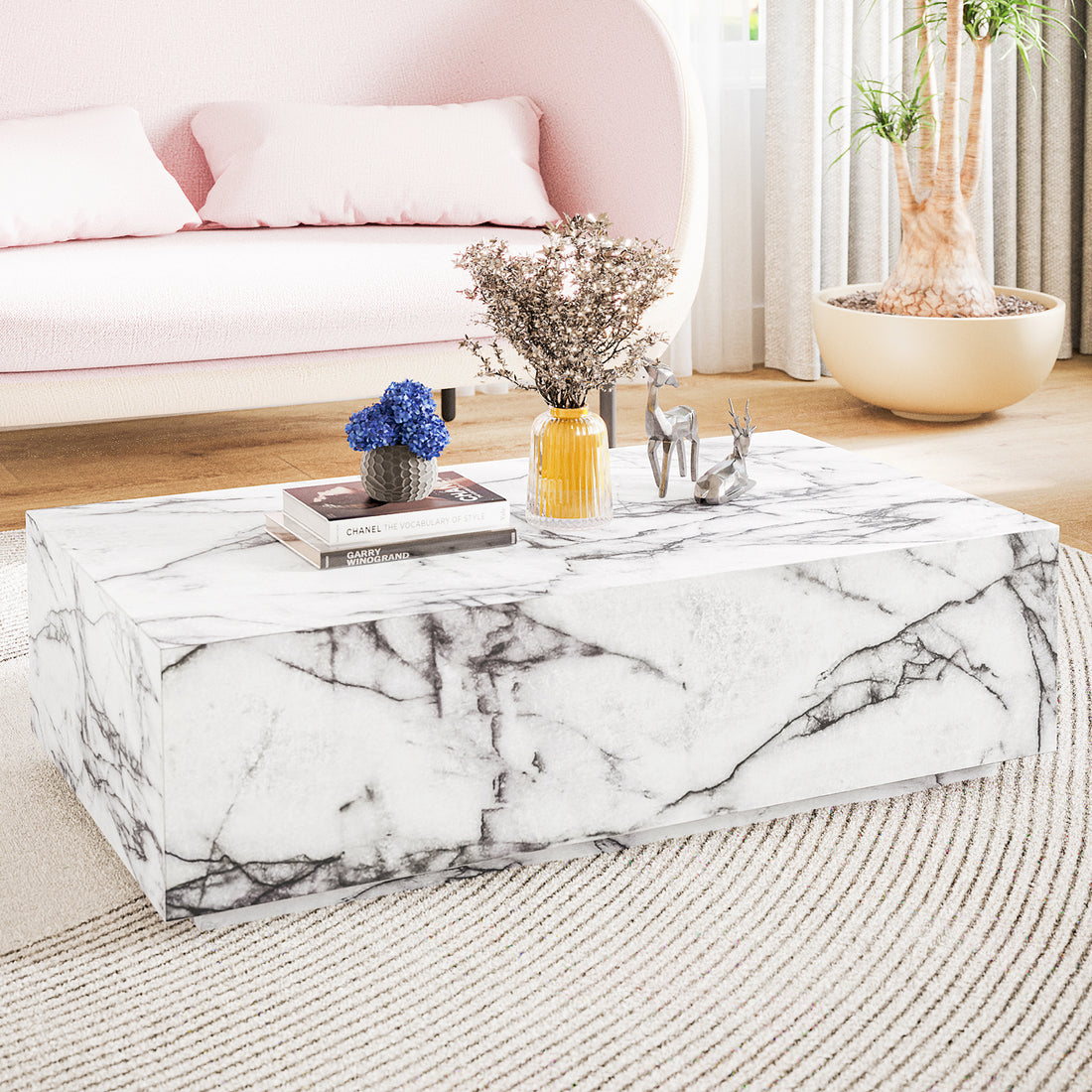 Parviz 88cm Rectangular Coffee Table in Marble, featuring a sleek marble finish with books, a charcoal pot of blue flowers, an amber vase, and metallic deer figurines, complements the pale-pink sofa.