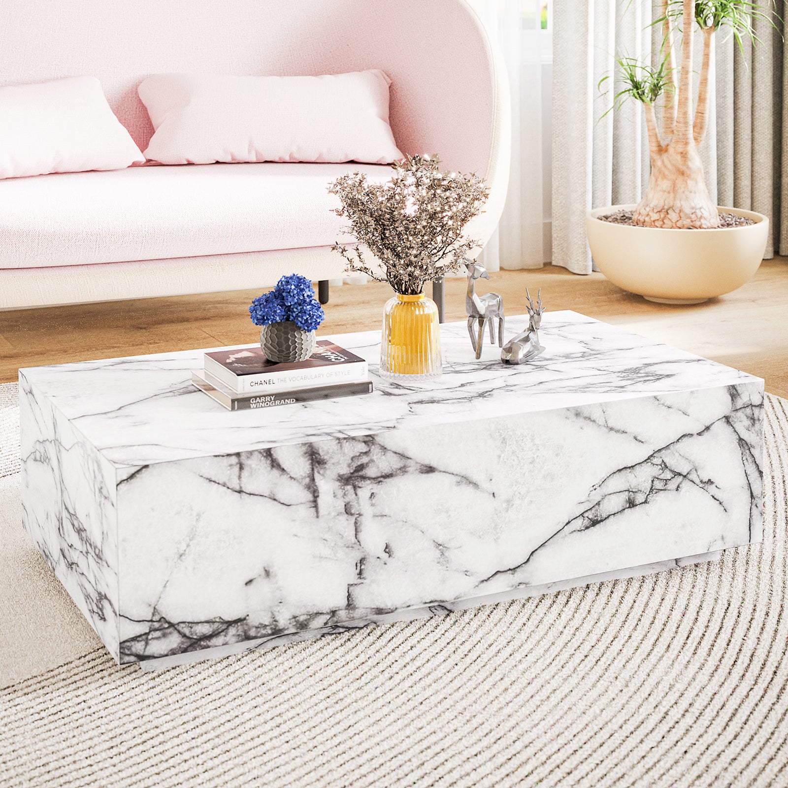 Parviz 88cm Rectangular Coffee Table in Marble, featuring a sleek marble finish with books, a charcoal pot of blue flowers, an amber vase, and metallic deer figurines, complements the pale-pink sofa.