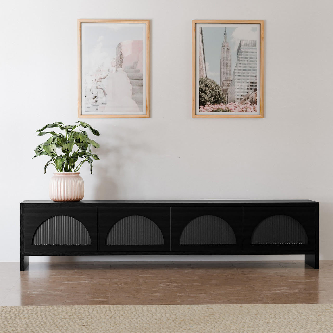 Philippe 200cm Arch Door TV Entertainment Unit in Black with subtle half-circle grooves, flanked by a pink planter, under two light-wood framed prints, against a white wall.