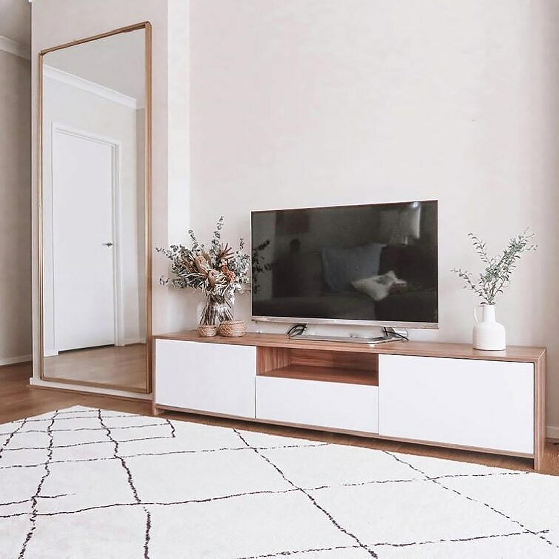 Rocco Entertainment Unit with Shelves in White, featuring sleek design, open shelf, smooth-gliding drawer, and enclosed cabinets, complements a minimalist living room setup with a TV and decor on top.
