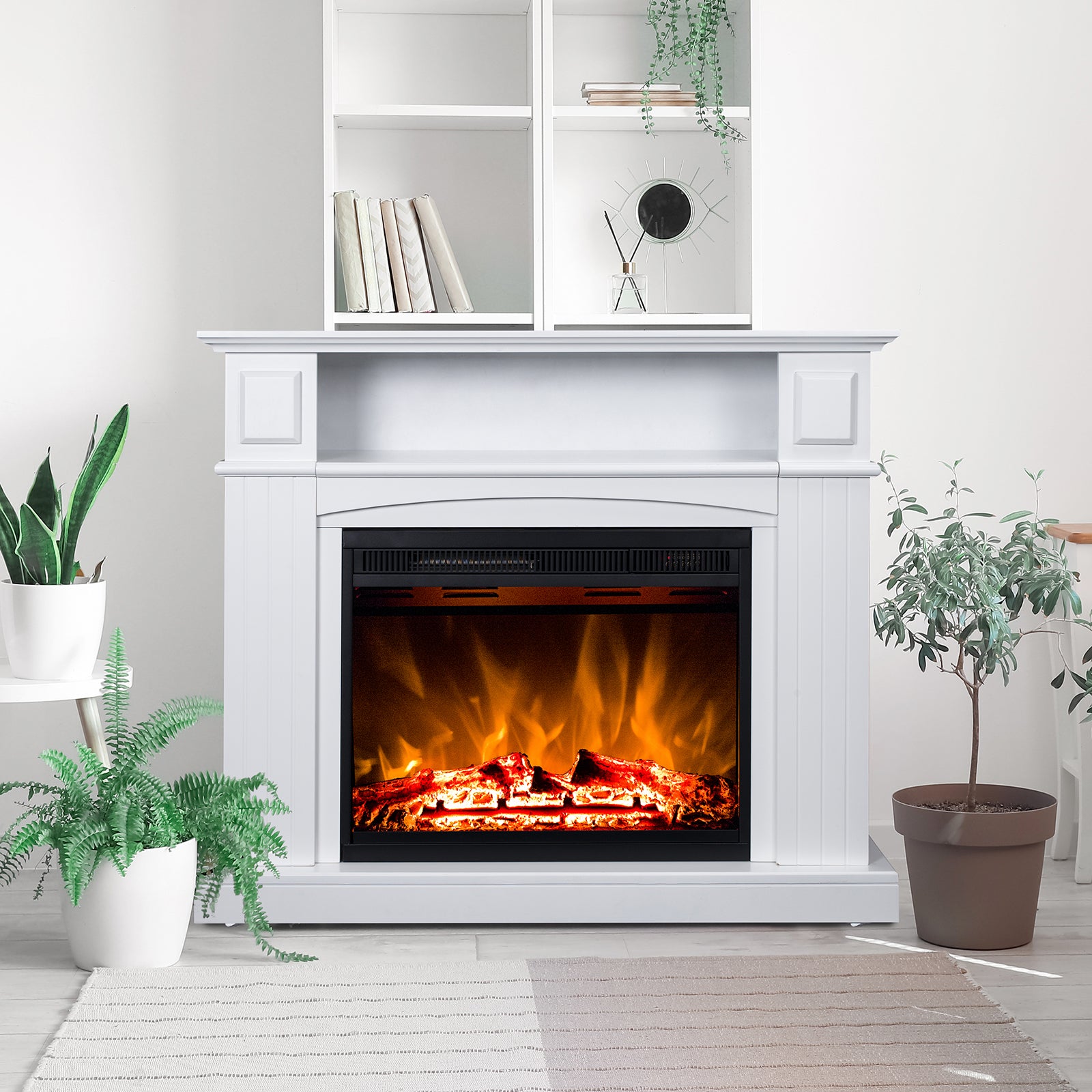 Banhi 1500W Electric Fireplace Heater with Mantel in White, featuring realistic LED flames, is flanked by potted plants and topped with books, a mirror, and a trailing plant on open shelves.