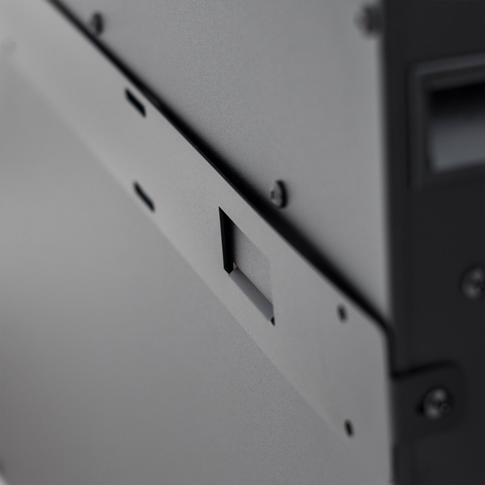 Close-up of Dakota 60 Wall Mounted 1500W Electric Fireplace Heater, showcasing a textured gray steel panel with a central latch and black screws, emphasizing its sleek, space-saving design.