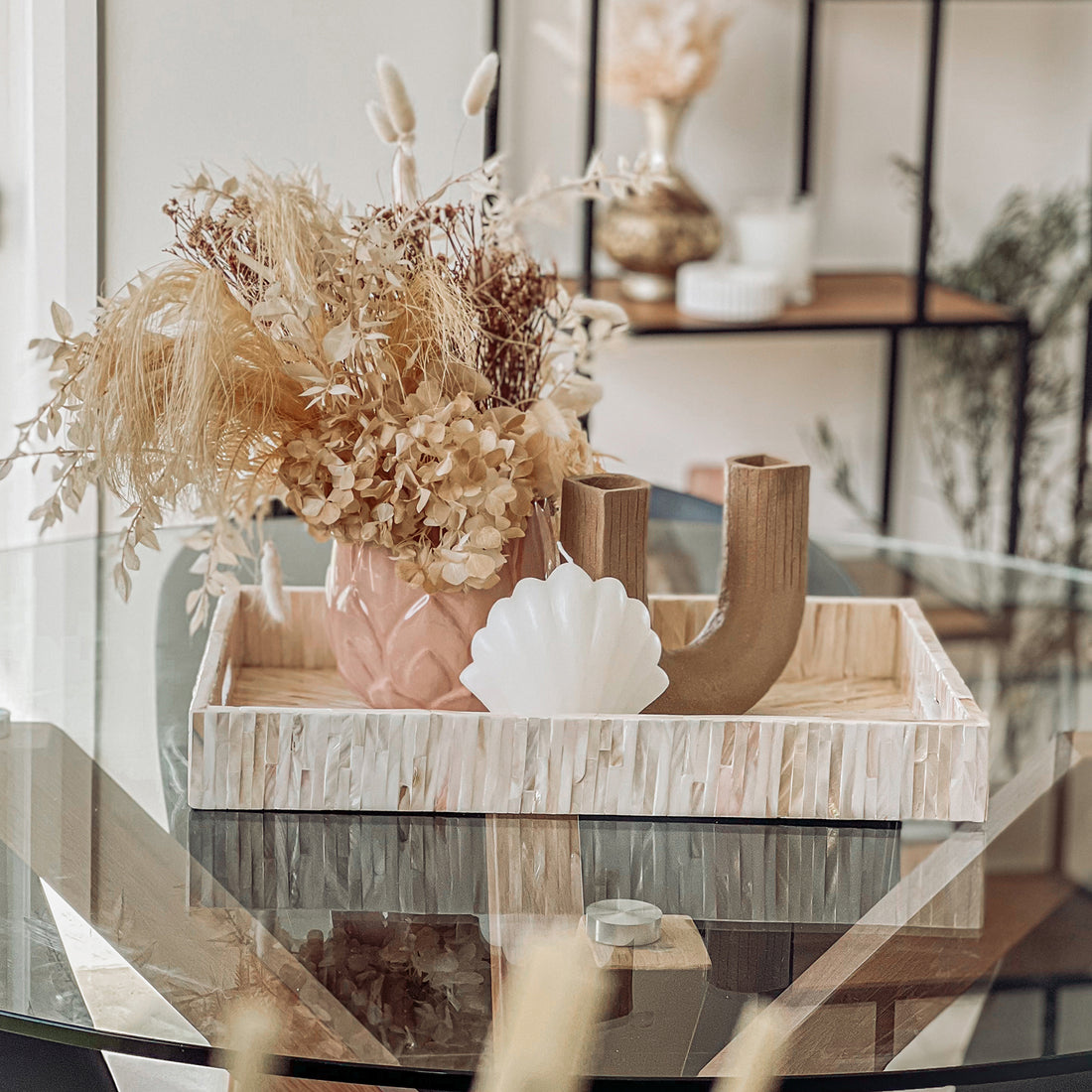 Nanaya 45cm Mother of Pearl Decorative Tray in Cream Beige on a glass table, featuring a pink ceramic vase with dried flowers, a shell-shaped candle, and a wooden U-shaped object.