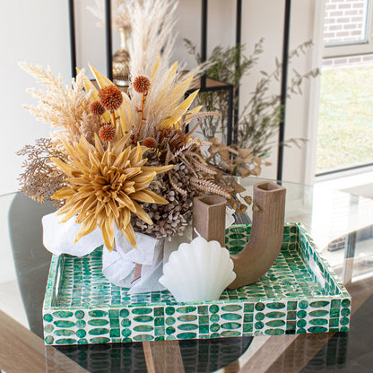 Nanaya 45cm Mother of Pearl Decorative Tray in Jade Green displayed with a dried floral bouquet, U-shaped ceramic candleholder, and shell-shaped candle on a glass-top table.
