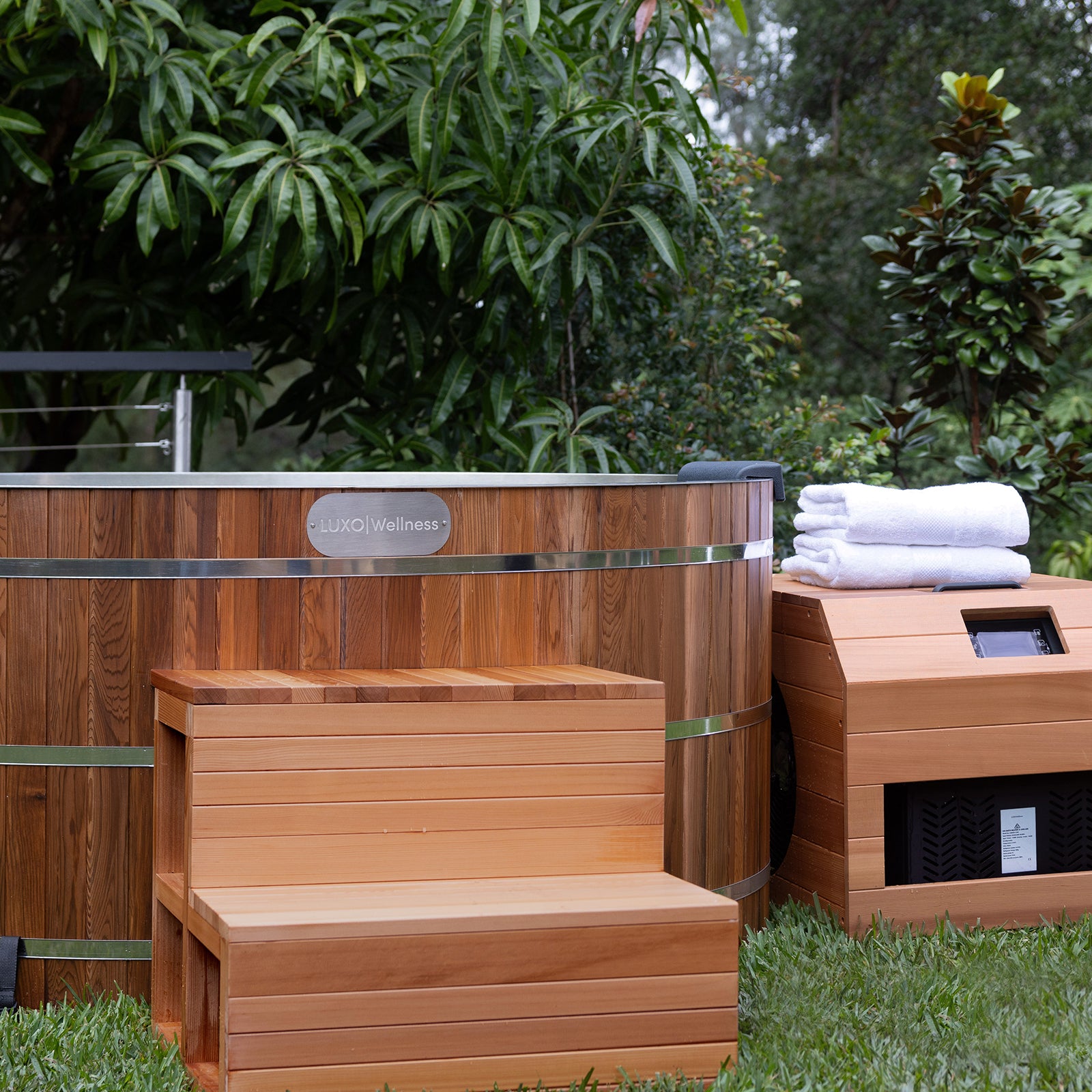 Denman 2 Person Outdoor Ice Bath with 1.5HP Chiller in Natural, features a barrel-style wooden tub on a lawn, accompanied by a matching two-step bench and equipment box with white towels.