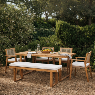 Albian 7 Seater Hardwood Outdoor Dining Set in Beige featuring a rectangular wooden table, four armchairs, a bench with cream cushions, citrus-filled bowl, carafe, and dining settings, nestled in lush greenery.