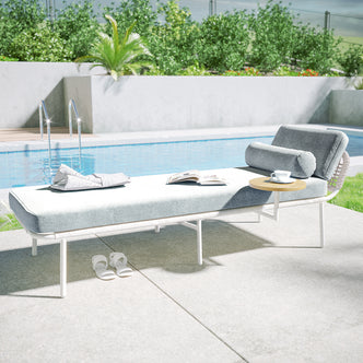 Andre Wicker Outdoor Sun Lounger Set of 2 in Light Grey beside a pool, featuring light-gray cushion, adjustable backrest, bolster pillow, attached side table with coffee cup, open magazine, and folded towel.