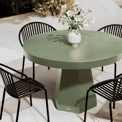 Apollo 120cm Outdoor Concrete Dining Table in Green with a round top and sturdy pedestal base, surrounded by four black metal chairs, featuring a white vase with flowers.