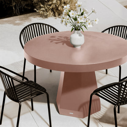Apollo 120cm Outdoor Concrete Dining Table in Mocha Mousse with a terracotta-pink hue, round design, and sculptural pedestal base, surrounded by black metal chairs on a stone patio.