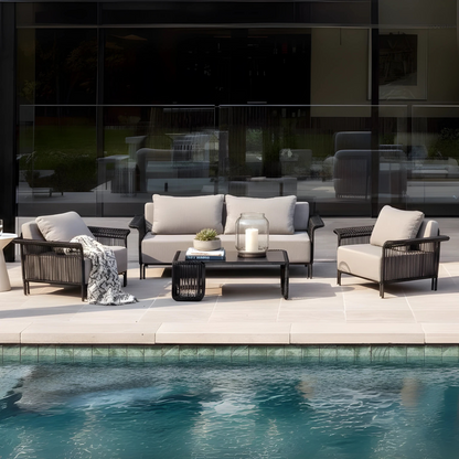 Avon 5 Seater Premium Rattan Outdoor Sofa Set in Grey features a two-seat sofa, two armchairs, and a black coffee table with a succulent, books, and candle, set on a poolside deck.