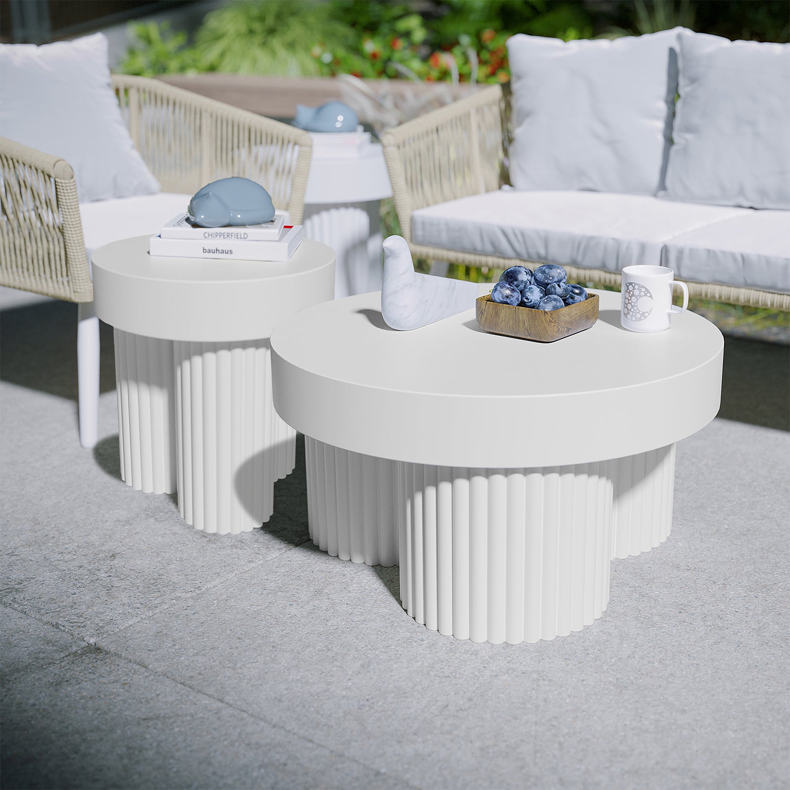 Basalt & Salvo Outdoor Concrete Coffee Table Set in White features two round tables with fluted bases, adorned with a marble bird sculpture, plums in a wooden bowl, and a patterned ceramic mug.