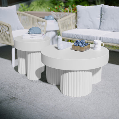 Basalt & Salvo Outdoor Concrete Coffee Table Set in White features two round tables with fluted bases, adorned with a marble bird sculpture, plums in a wooden bowl, and a patterned ceramic mug.