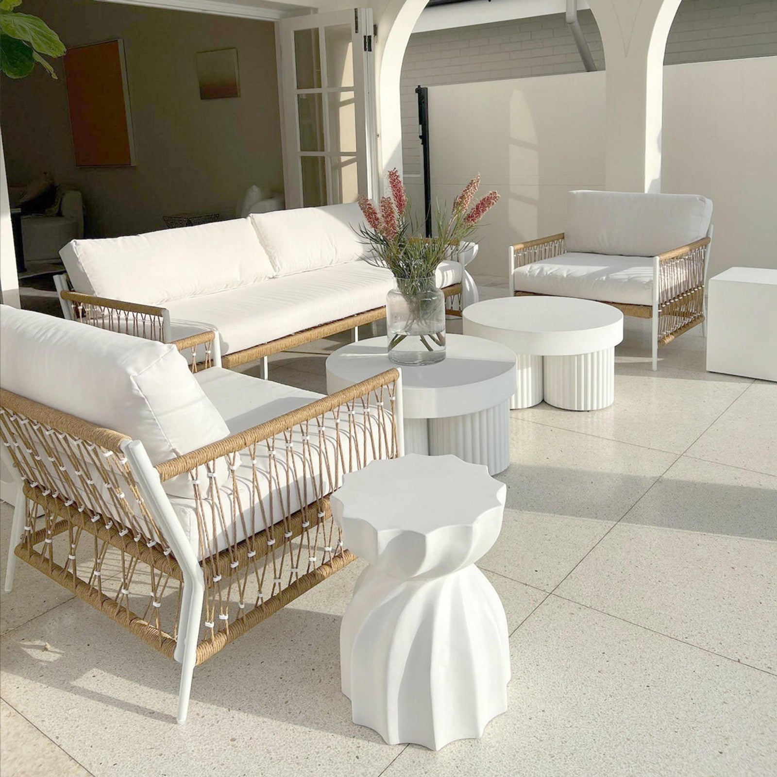 Basalt 70cm Indoor & Outdoor Concrete Coffee Table in White, with a smooth, cylindrical base, complements a minimalist patio. Features a clear vase with pinkish blooms, enhancing its modern appeal.