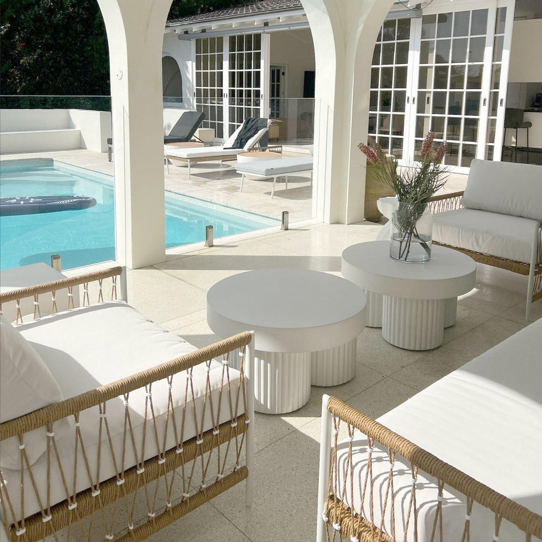 Basalt 70cm Indoor & Outdoor Concrete Coffee Table in White, featuring a minimalist design with a round shape and sturdy build, set in a bright, poolside lounge area with modern decor.