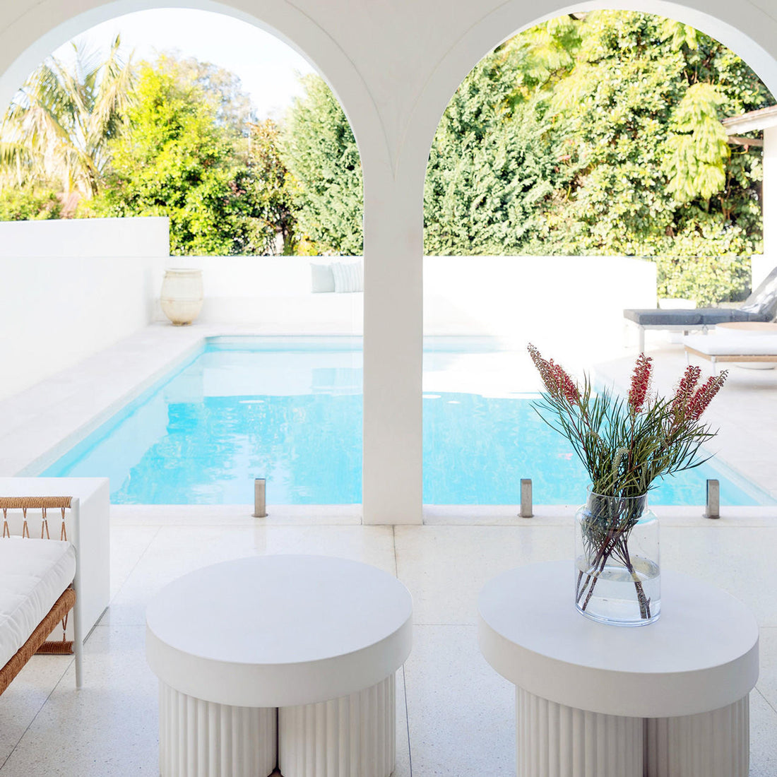 Basalt 70cm Indoor & Outdoor Concrete Coffee Table in White, situated in a minimalist outdoor lounge with a pool, featuring a durable round design, blending seamlessly with the elegant, resort-like setting.