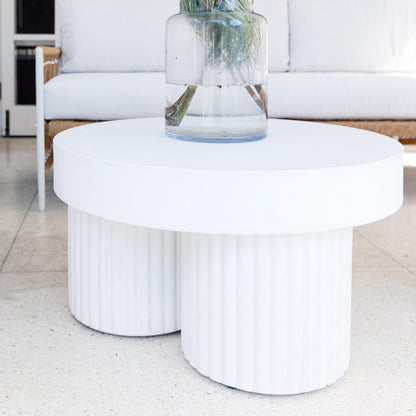 Basalt 70cm Indoor & Outdoor Concrete Coffee Table in White, featuring a round white top supported by fluted cylindrical bases, shown with a clear vase and green foliage on a terrazzo floor.