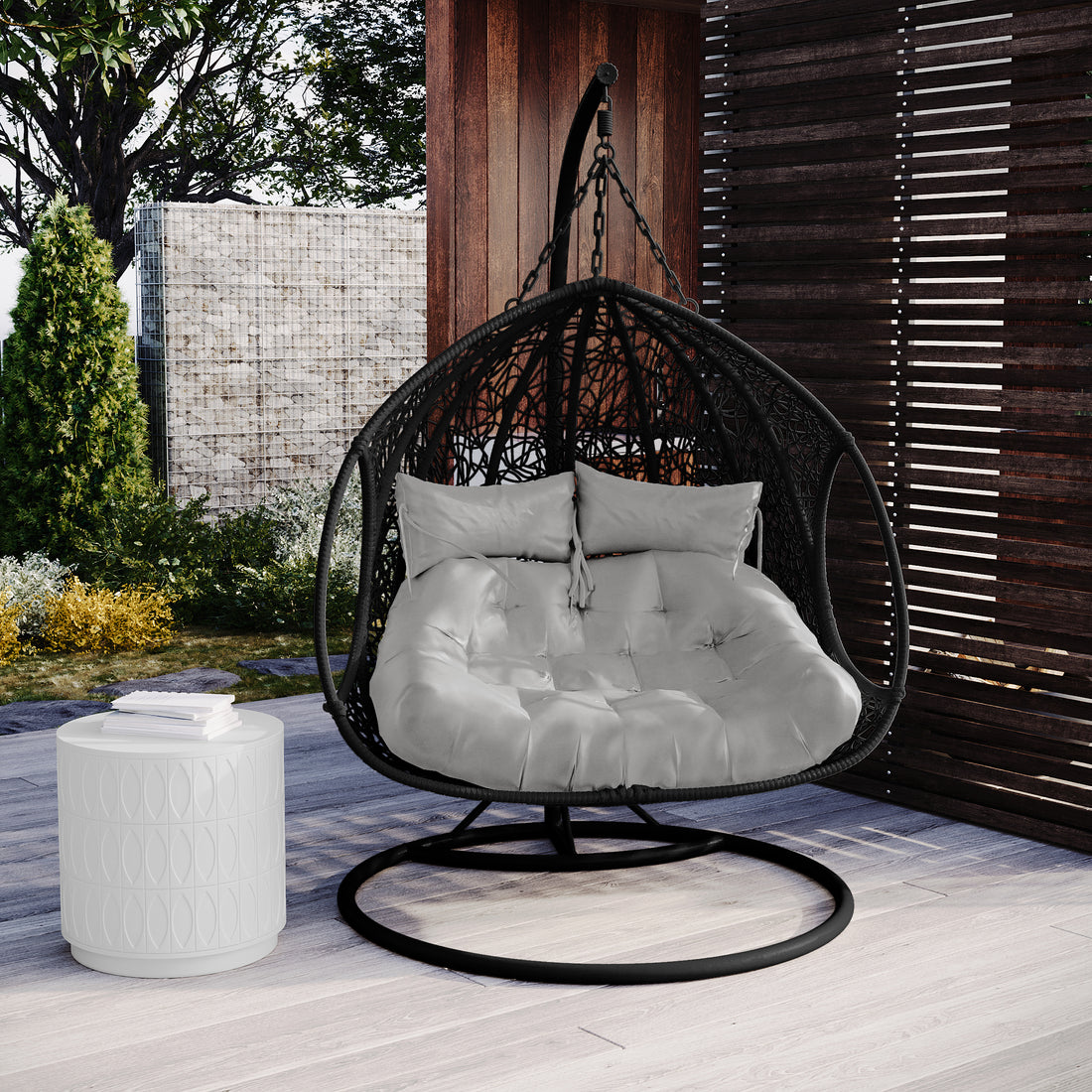 Basin 2-Seater Hanging Egg Chair with Cushion in Black, featuring a black metal frame and plush tufted cushion, centrally placed on a wooden deck with an elegant outdoor setting.