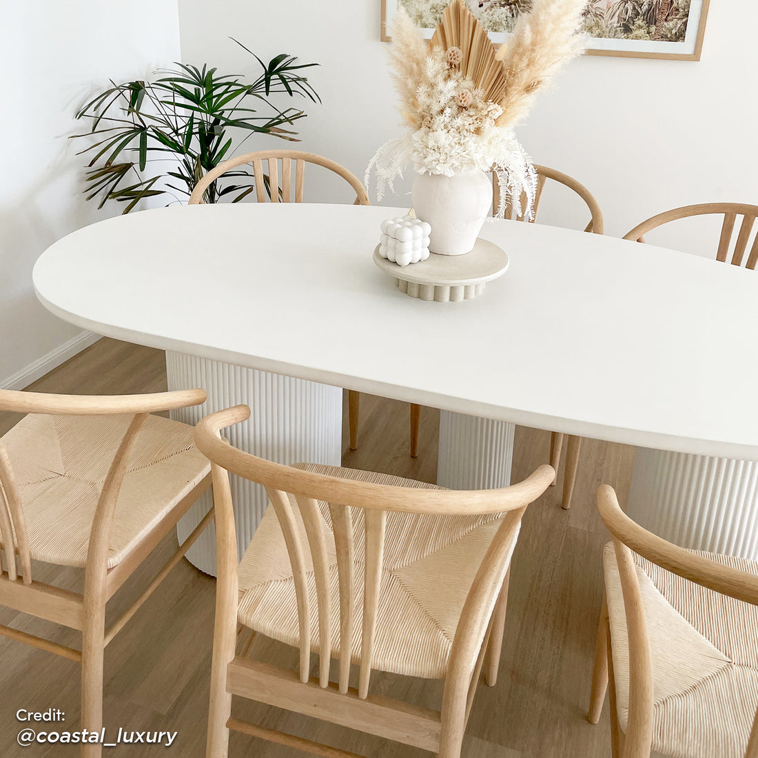 Belmar 200cm Concrete Indoor/Outdoor Dining Table in White, featuring an oval top with fluted pedestal legs, surrounded by Scandinavian-style chairs, styled with a vase of dried botanicals and a bubble candle.