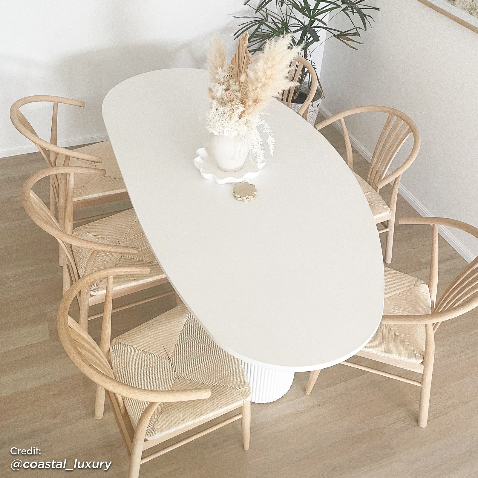 Belmar 200cm Curved Outdoor Concrete Dining Table in White, featuring an oval tabletop on a fluted pedestal base, styled with a sculptural tray and dried floral arrangement.