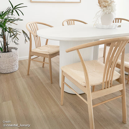 Belmar 200cm Curved Outdoor Concrete Dining Table in White, featuring a sleek, minimalist design, set in an airy dining nook with surrounding bent-wood chairs and a woven basket planter.