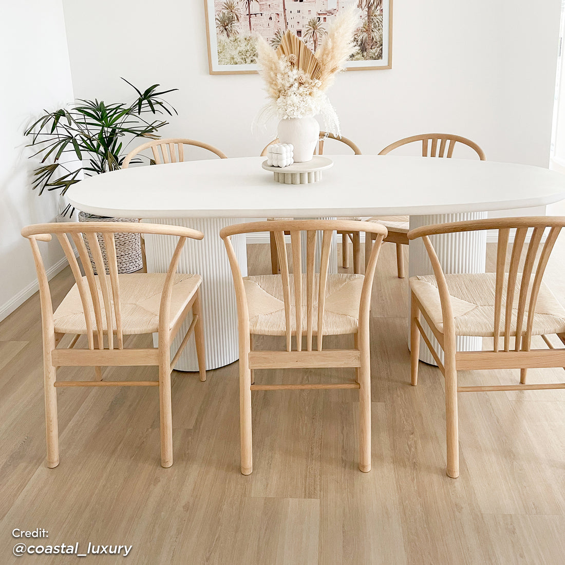 Belmar 200cm Curved Outdoor Concrete Dining Table in White, featuring an elegant oval shape and ribbed pedestal base, surrounded by six light-oak chairs with woven seats in a minimalist coastal-modern dining area.