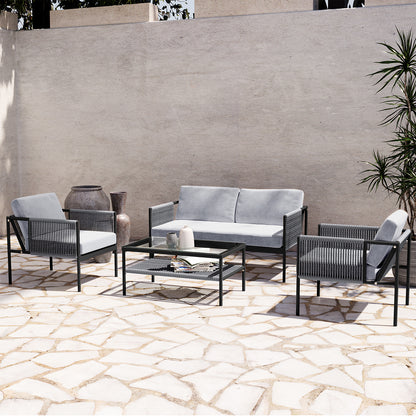 Brujas 4 Seater Wicker Outdoor Lounge Set in Grey, featuring a two-seat sofa, two armchairs, and a glass-top coffee table, elegantly arranged on a sunlit patio with decorative vases and greenery.