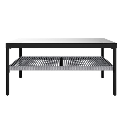 Brujas 4 Seater Wicker Outdoor Lounge Set in Grey features a sleek coffee table with a slim black metal frame, clear glass top, and a lower shelf of tightly woven grey rope slats.