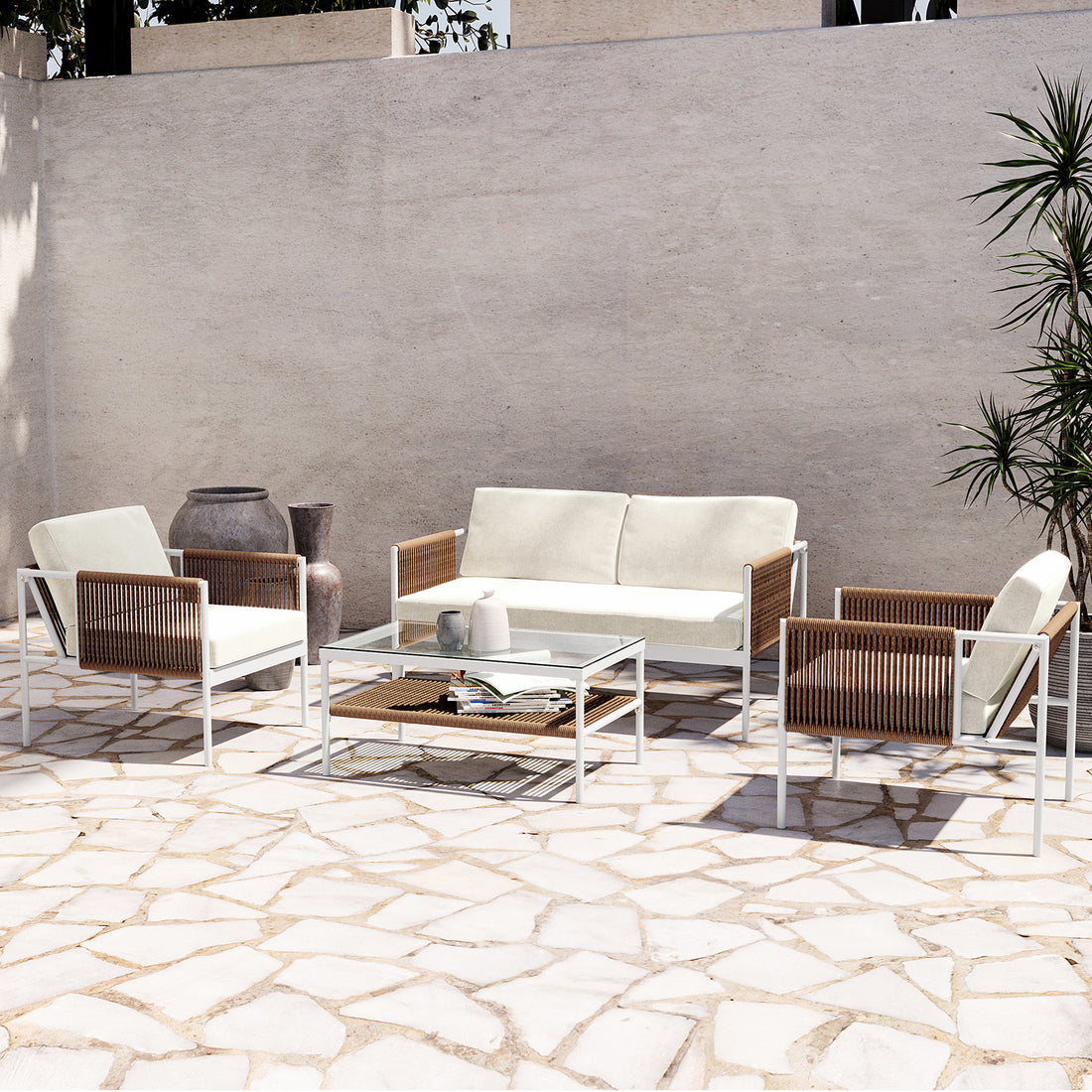 Brujas 4 Seater Wicker Outdoor Lounge Set in Light Beige features a two-seat sofa, two armchairs with white cushions, and a glass-topped coffee table on a sunlit stone patio.