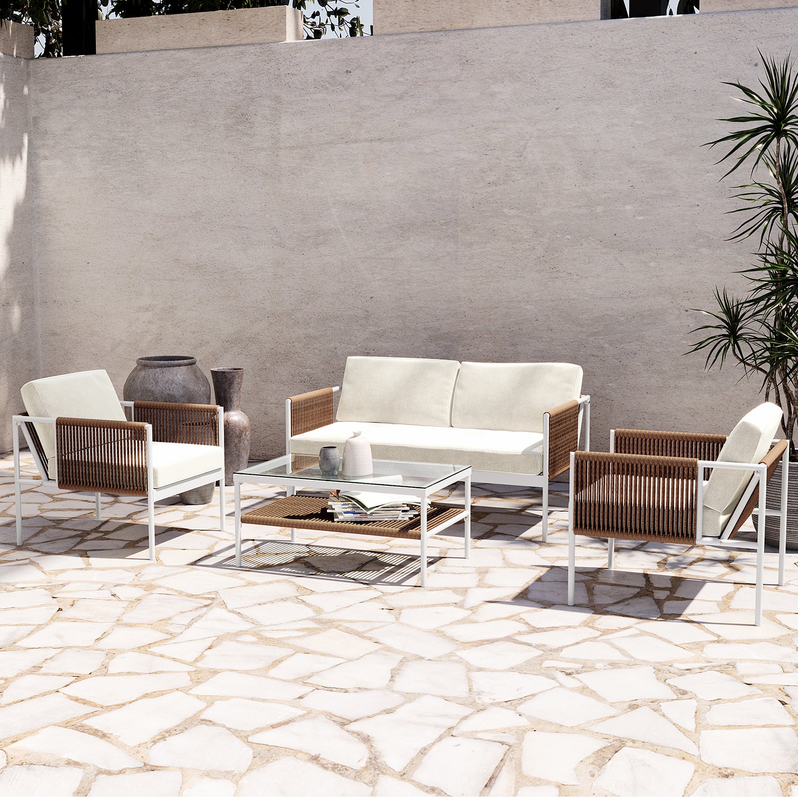 Brujas 4 Seater Wicker Outdoor Lounge Set in Light Beige features a two-seat sofa, two armchairs with white cushions, and a glass-topped coffee table on a sunlit stone patio.