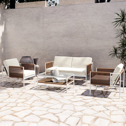 Brujas 4 Seater Wicker Outdoor Lounge Set in Light Beige features a two-seat sofa, two armchairs with white cushions, and a glass-topped coffee table on a sunlit stone patio.