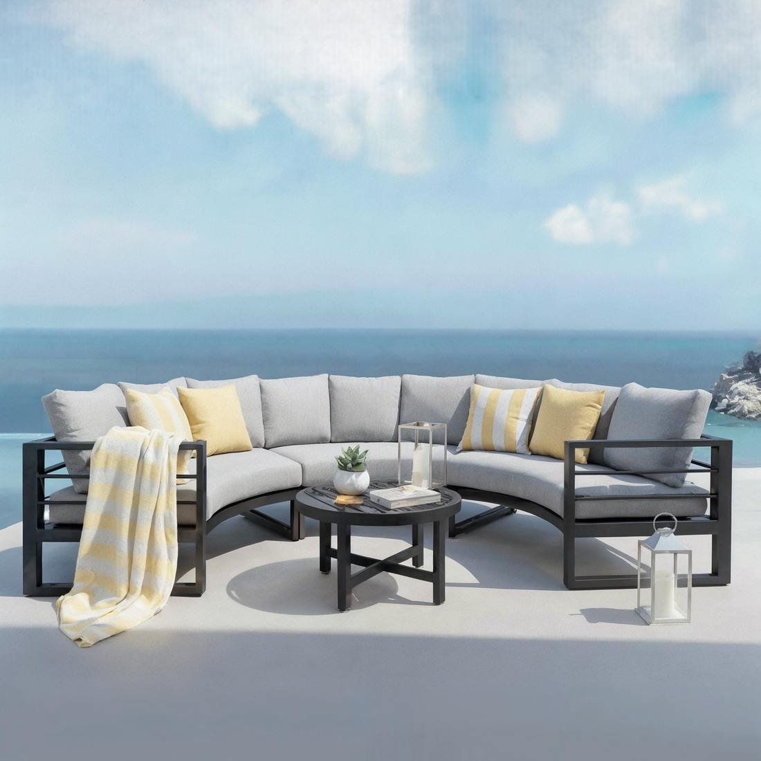 Callanna 5 Seater Curved Outdoor Lounge Set in Dark Grey features a modular sectional sofa with light-gray cushions, a round black coffee table, and accents like pillows and a striped throw blanket.