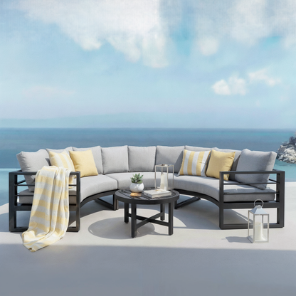 Callanna 5 Seater Curved Outdoor Lounge Set in Dark Grey features a modular sectional sofa with light-gray cushions, a round black coffee table, and accents like pillows and a striped throw blanket.
