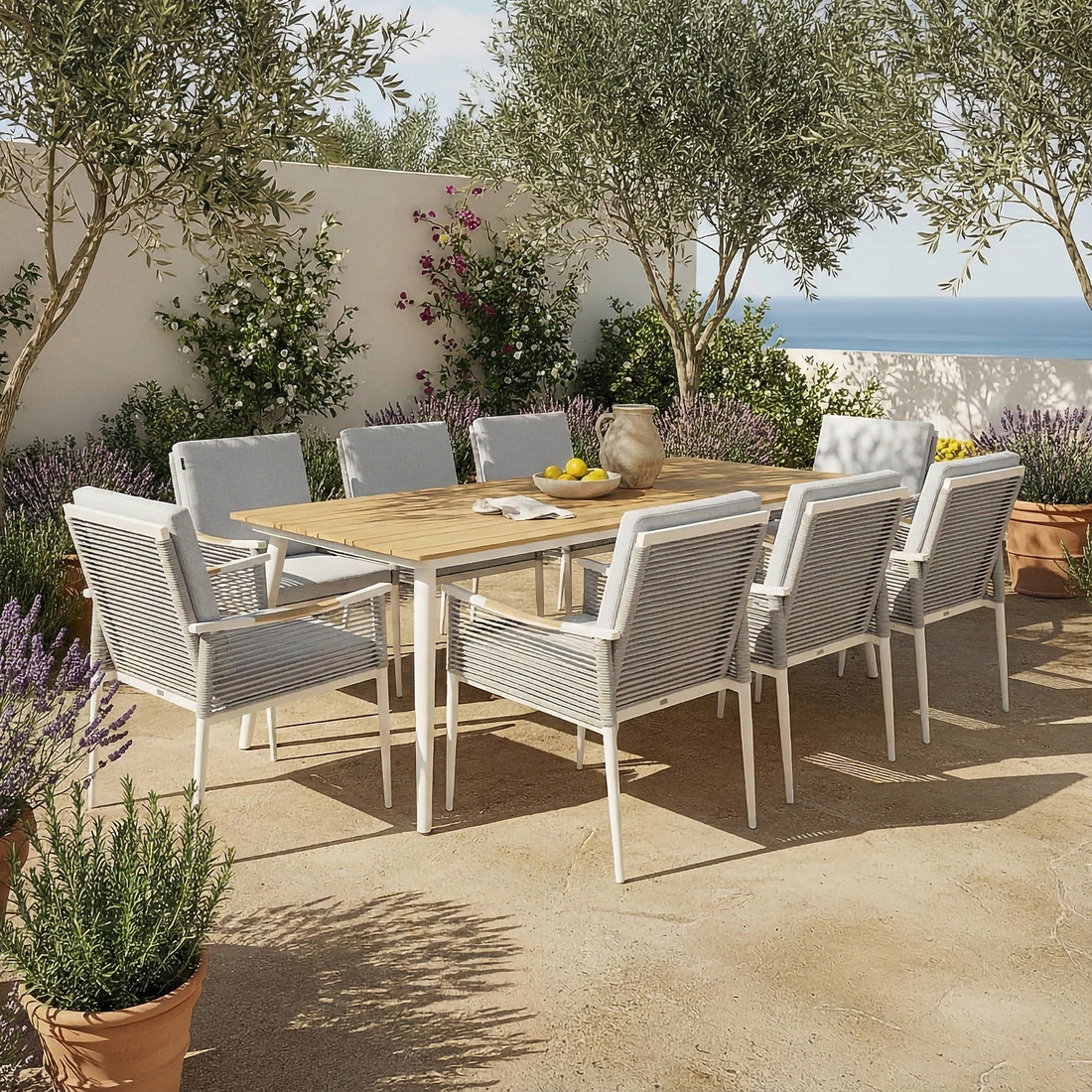 Casara 9 Piece Outdoor Dining Set in White and Grey features a wooden table with rope-wrapped armchairs on a sunlit Mediterranean terrace, surrounded by terracotta pots with lush plants.