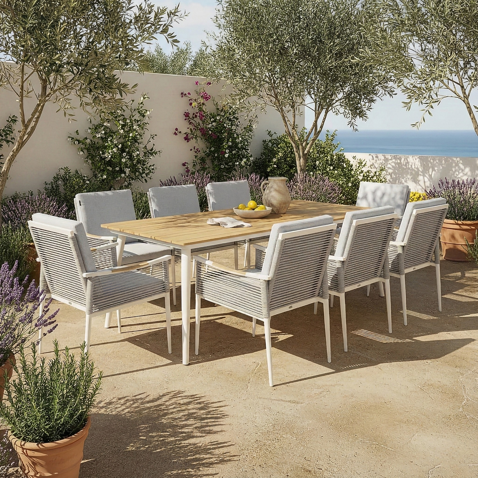 Casara 9 Piece Outdoor Dining Set in White and Grey features a wooden table with rope-wrapped armchairs on a sunlit Mediterranean terrace, surrounded by terracotta pots with lush plants.
