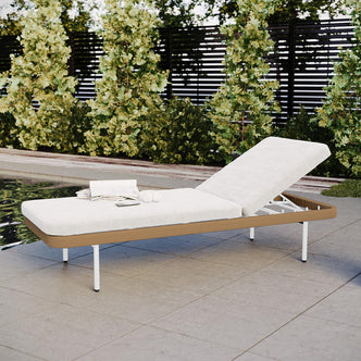 Culion Wicker & Aluminium Outdoor Sun Lounger in Light Beige featuring an angled backrest, white cushion, light brown frame, slender legs, with an open magazine, headphones, and smartphone on the seat.