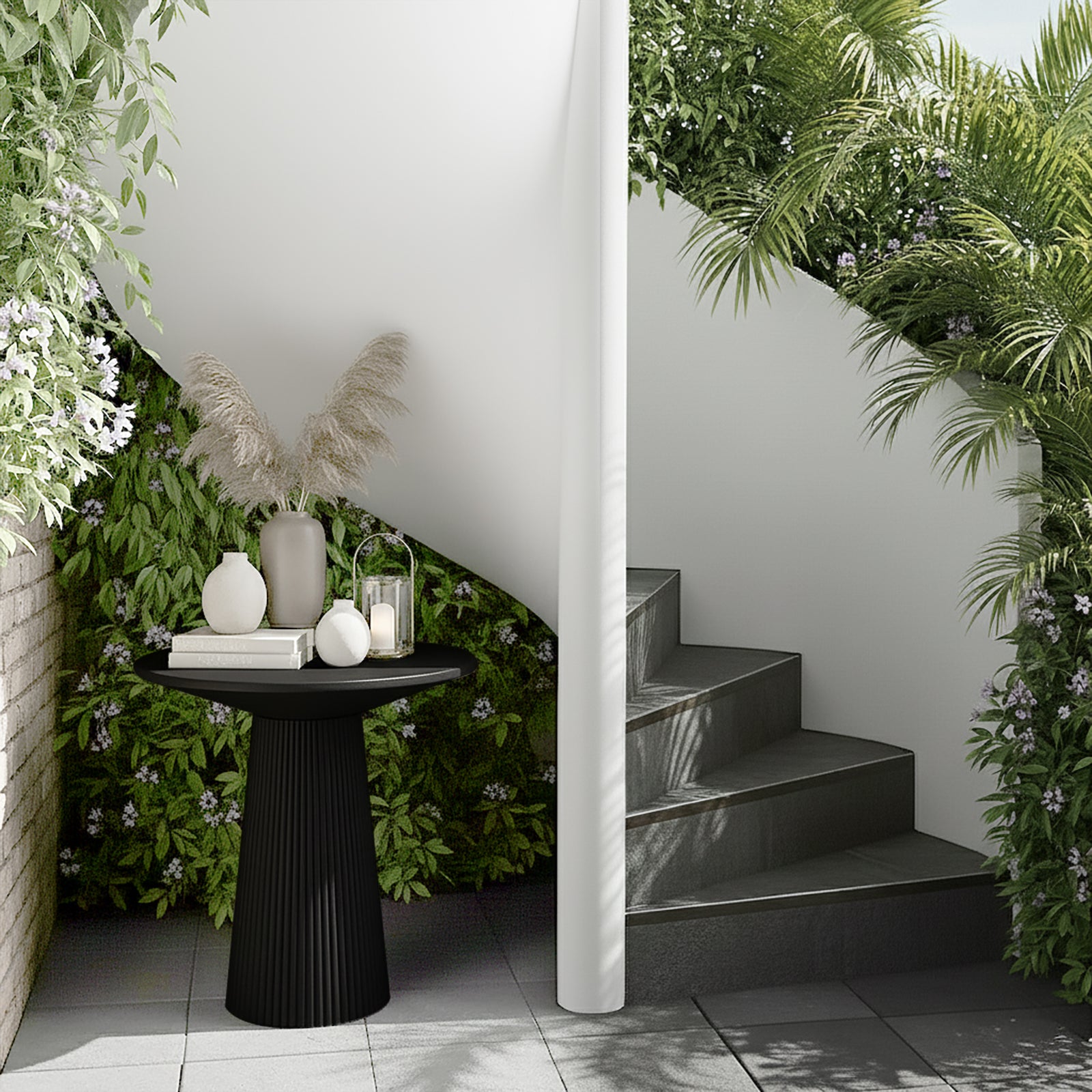 Darien 80cm Round Concrete Hallway Table in Grey Marble with a fluted base, topped with a matte-gray vase, ceramic vases, books, and a glass lantern, set in a lush patio corner.