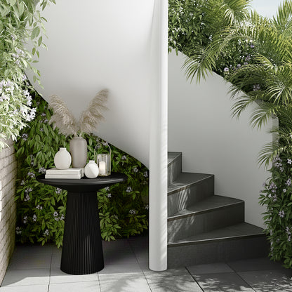 Darien 80cm Round Concrete Hallway Table in Grey Marble with a fluted base, topped with a matte-gray vase, ceramic vases, books, and a glass lantern, set in a lush patio corner.