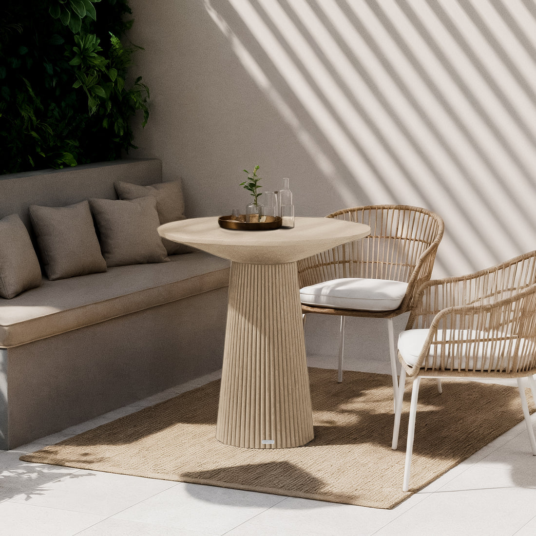 Darien 80cm Round Concrete Bistro Table in Ivory, featuring a fluted base and smooth top, sits elegantly in a sunlit nook with woven rattan chairs and a natural-fiber rug.