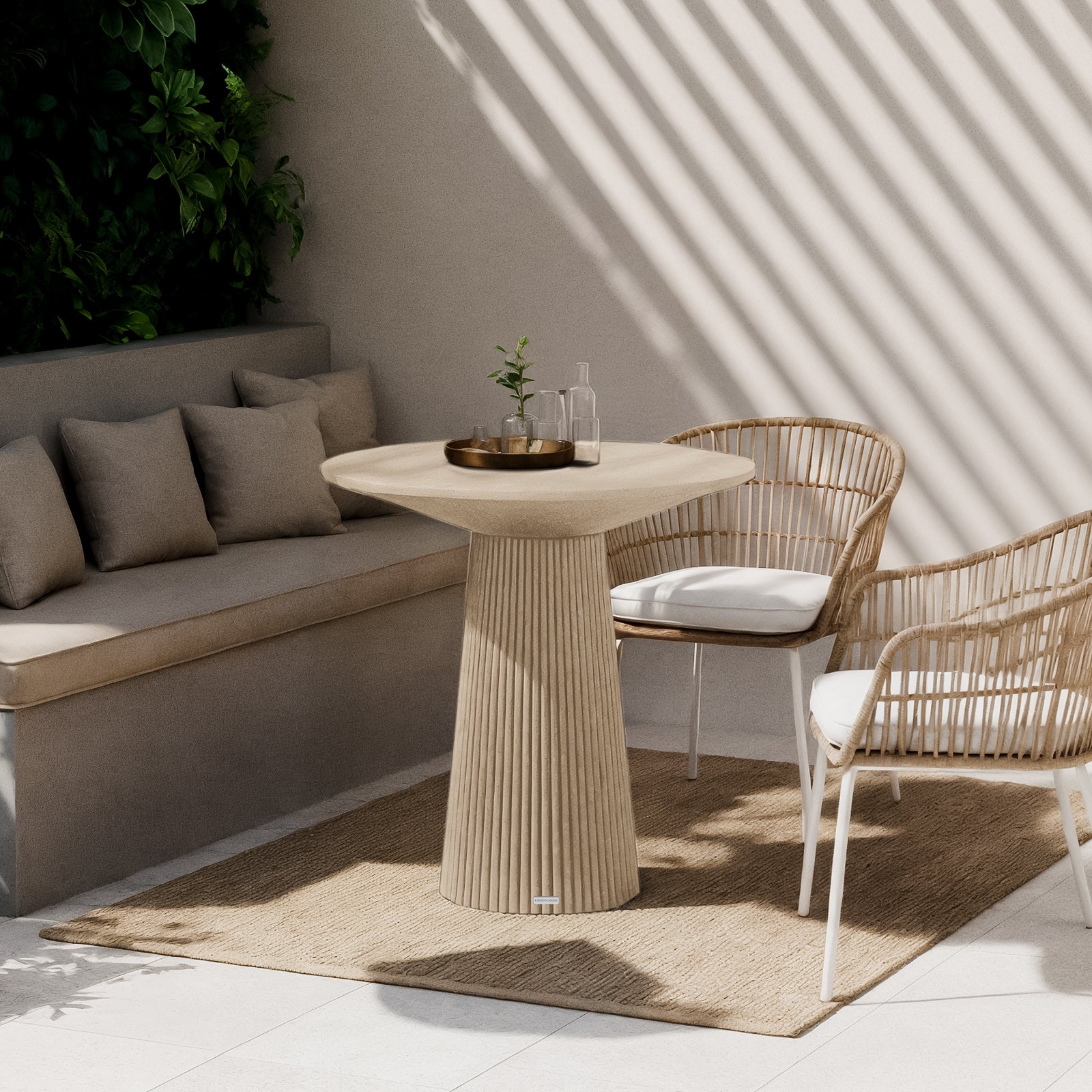 Darien 80cm Round Concrete Bistro Table in Ivory, featuring a fluted base and smooth top, sits elegantly in a sunlit nook with woven rattan chairs and a natural-fiber rug.