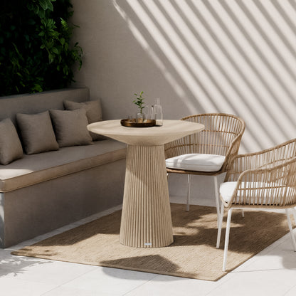 Darien 80cm Round Concrete Bistro Table in Ivory, featuring a fluted base and smooth top, sits elegantly in a sunlit nook with woven rattan chairs and a natural-fiber rug.