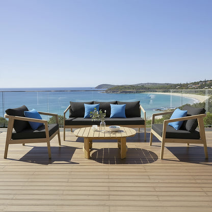 Delva 4 Seater Hardwood Acacia Outdoor Sofa Set in Black, featuring a two-seat sofa, two armchairs with charcoal cushions, and a round coffee table, set on a sunny coastal deck.
