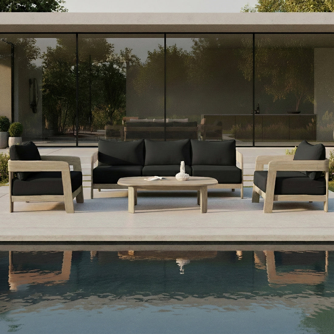 Elani 5 Seater Acacia Hardwood Outdoor Sofa Set in Black features a wooden-frame sofa and armchairs with black cushions, arranged around an oval coffee table on a sleek concrete terrace.