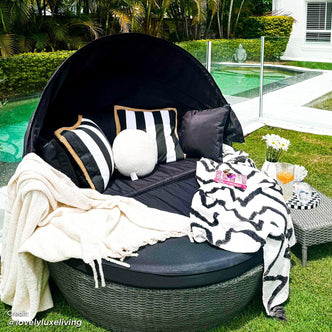 Erith Wicker Outdoor Furniture Day Bed w/ Canopy featuring a close-up of a striped pillow, bouquet of flowers, and canopy, highlighting its luxurious design and inviting lounging space.