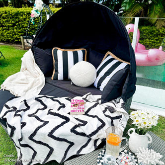Erith Wicker Outdoor Furniture Day Bed w/ Canopy features a plush, striped pillow and soft blanket, complemented by a nearby vase of flowers, highlighting a cozy outdoor relaxation setup.