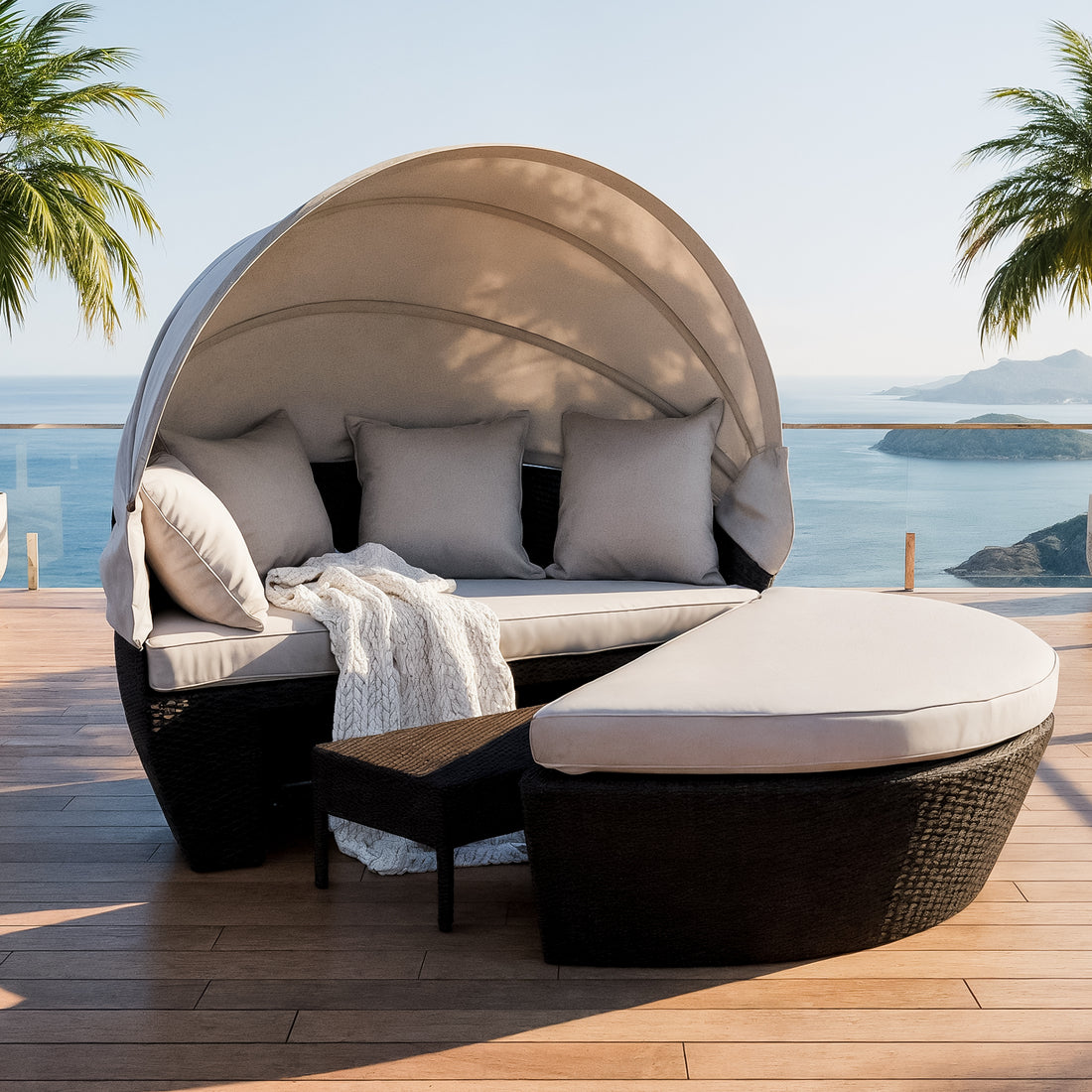 Erith Round Wicker Outdoor Daybed in Light Grey & Black features a semi-circular wicker design with a canopy, light-beige cushions, throw pillows, and a matching ottoman on a seaside deck.